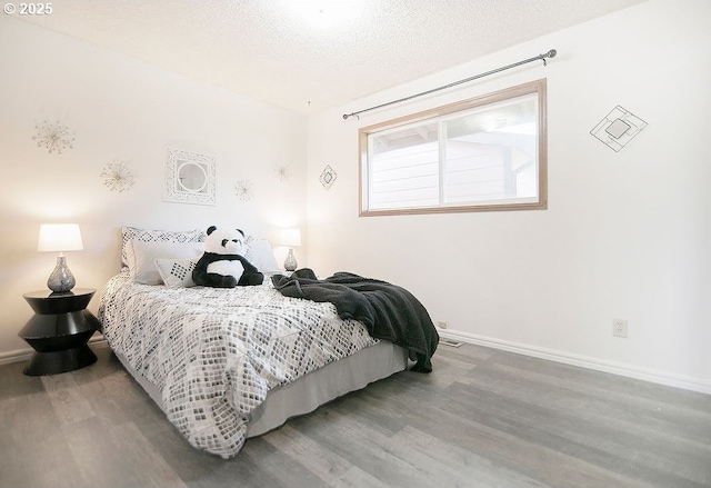 bedroom with a textured ceiling, wood finished floors, and baseboards