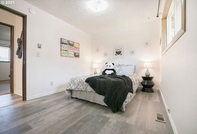 bedroom with visible vents, a textured ceiling, baseboards, and wood finished floors