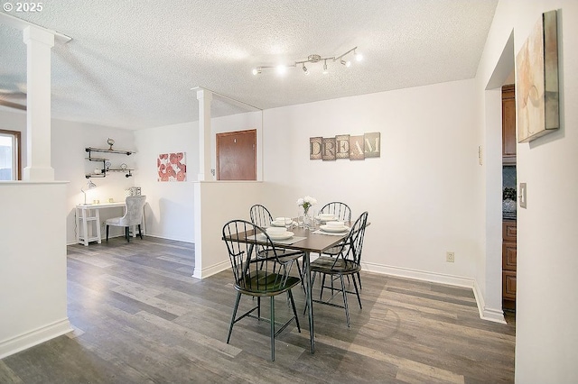 dining area featuring ornate columns, a textured ceiling, baseboards, and wood finished floors