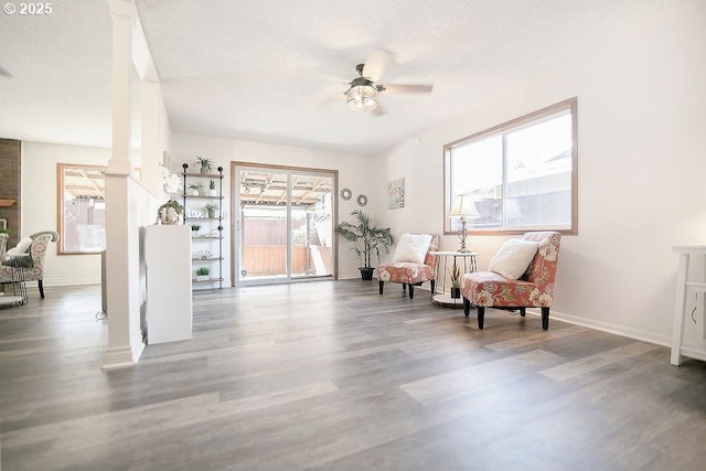 living area with decorative columns, ceiling fan, a textured ceiling, wood finished floors, and baseboards