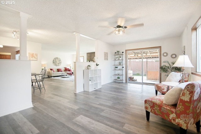 living area with ceiling fan, a textured ceiling, ornate columns, and wood finished floors