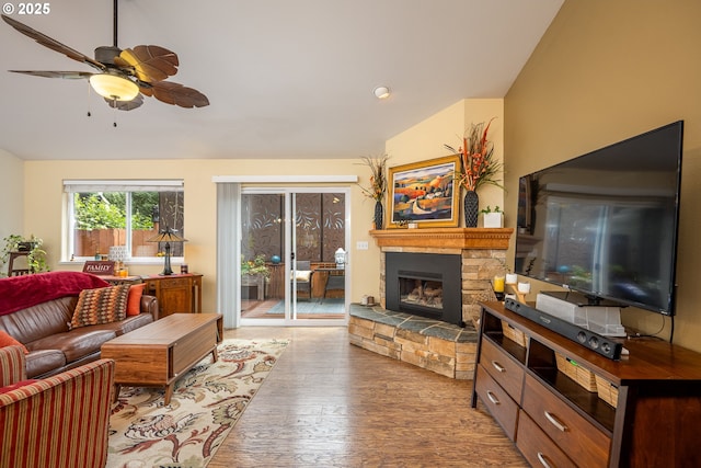 living area with ceiling fan, vaulted ceiling, wood-type flooring, and a stone fireplace
