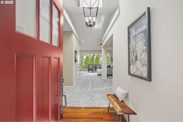 carpeted entrance foyer with ceiling fan with notable chandelier, wood finished floors, and baseboards