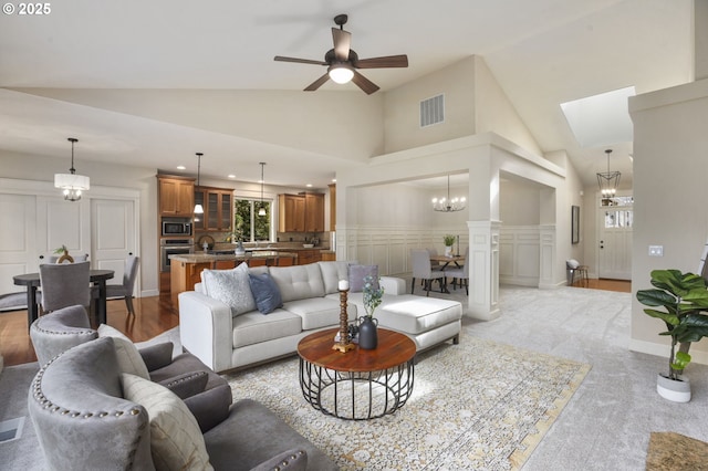 living room featuring high vaulted ceiling, visible vents, a decorative wall, and ceiling fan with notable chandelier