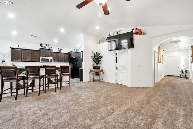 living area with lofted ceiling, visible vents, light carpet, arched walkways, and ceiling fan