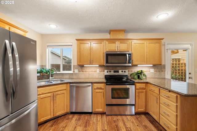 kitchen featuring light wood finished floors, a peninsula, a sink, stainless steel appliances, and tasteful backsplash