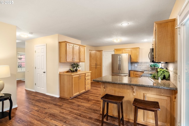 kitchen with tasteful backsplash, light brown cabinets, appliances with stainless steel finishes, a peninsula, and dark wood-style flooring