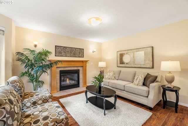 living area with a tiled fireplace, baseboards, and wood finished floors