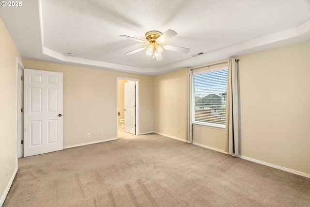 empty room featuring visible vents, a tray ceiling, carpet floors, baseboards, and ceiling fan