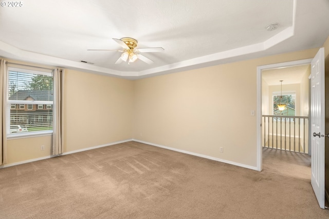 carpeted empty room with a tray ceiling, a ceiling fan, baseboards, and visible vents