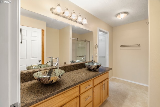 full bath featuring a sink, an enclosed shower, baseboards, and double vanity