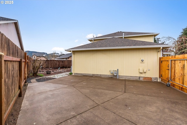 view of home's exterior with a patio area, a fenced backyard, and a shingled roof