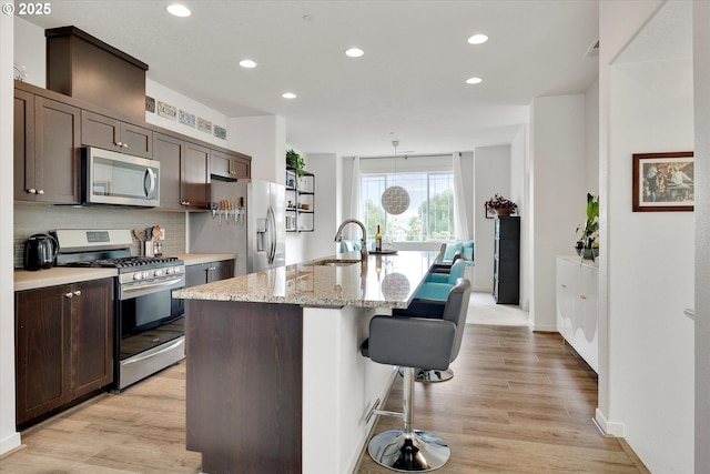 28671 SW Orleans Ave, Wilsonville, OR 97070 - kitchen featuring appliances with stainless steel finishes, a sink, a kitchen island with sink, tasteful backsplash, and a kitchen bar