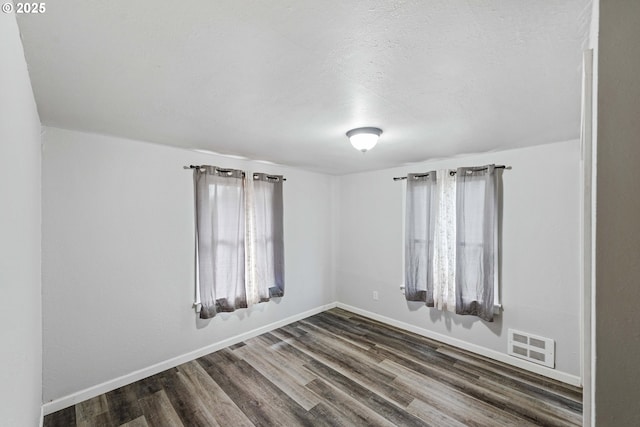 unfurnished room featuring visible vents, baseboards, a textured ceiling, and dark wood-style floors