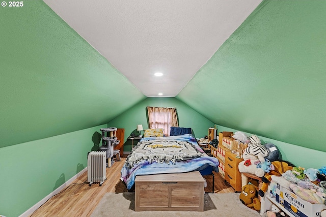 bedroom with lofted ceiling, a textured ceiling, wood finished floors, radiator, and baseboards