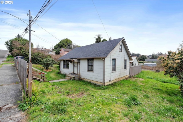 bungalow featuring a shingled roof, a front lawn, and fence