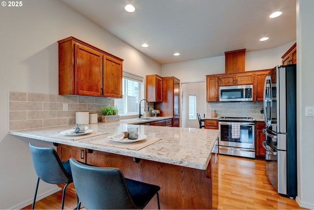 kitchen with stainless steel appliances, light wood-type flooring, a sink, and a peninsula