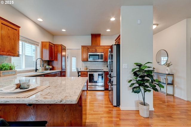 kitchen with light stone counters, a peninsula, stainless steel appliances, light wood-type flooring, and a sink