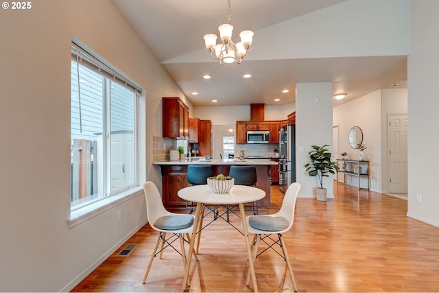 dining space featuring light wood finished floors, visible vents, an inviting chandelier, vaulted ceiling, and baseboards