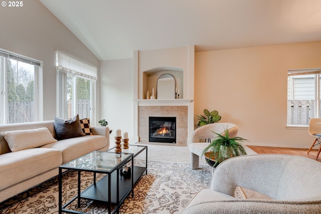 living room featuring baseboards, vaulted ceiling, a wealth of natural light, and a tile fireplace