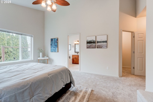 bedroom featuring light carpet, baseboards, ensuite bath, ceiling fan, and a high ceiling