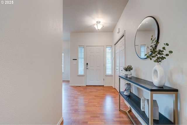 foyer entrance with baseboards, wood finished floors, and a textured wall