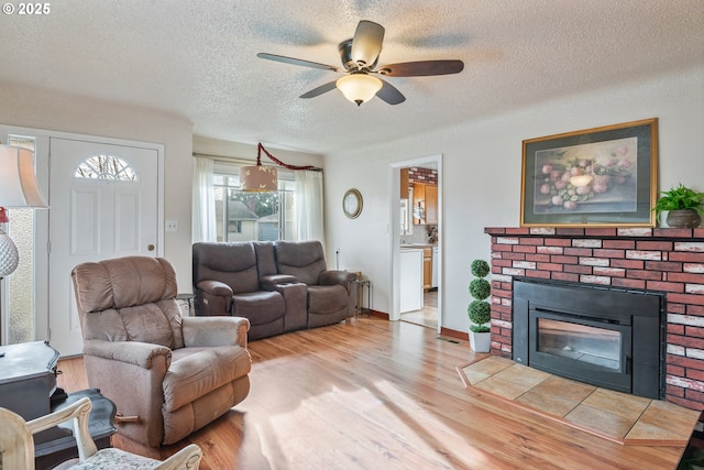 living room with ceiling fan, a fireplace, light hardwood / wood-style flooring, and a textured ceiling