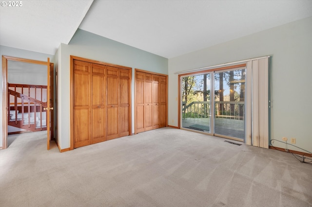 unfurnished bedroom featuring two closets, light colored carpet, visible vents, access to outside, and baseboards