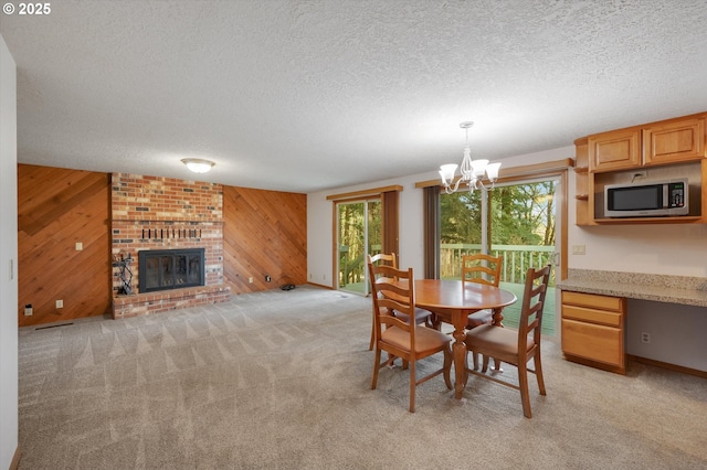 dining area featuring a textured ceiling, a chandelier, wooden walls, light carpet, and a fireplace