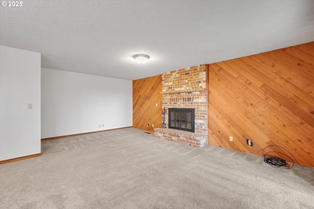 unfurnished living room featuring a textured ceiling, a brick fireplace, carpet flooring, and wooden walls