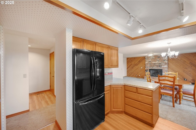 kitchen with light wood finished floors, freestanding refrigerator, a brick fireplace, track lighting, and a peninsula