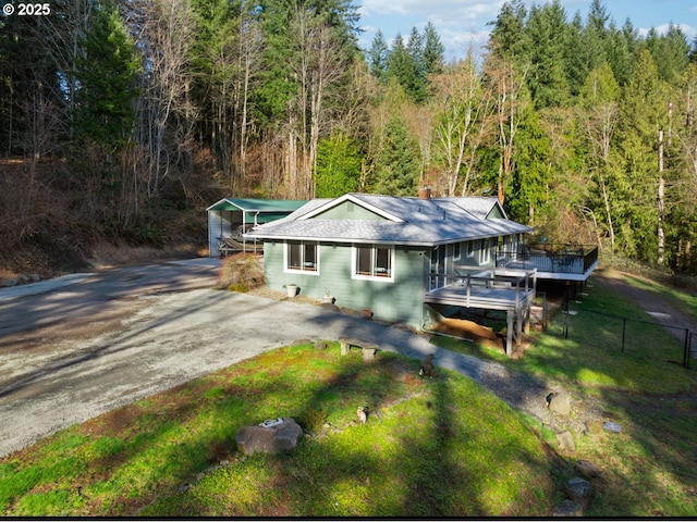 view of front facade with driveway, a forest view, fence, a wooden deck, and a front lawn