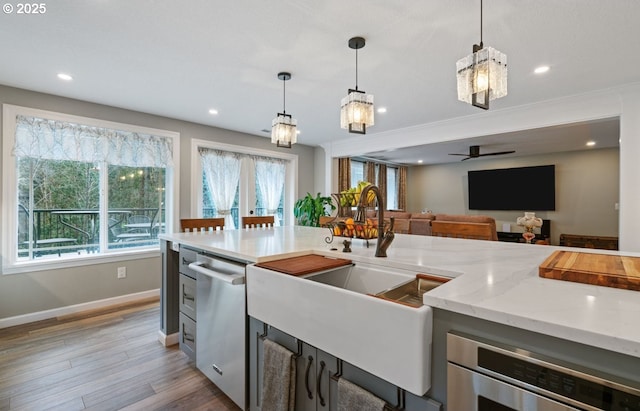 kitchen with light wood finished floors, dishwasher, light stone countertops, pendant lighting, and a sink