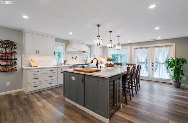 kitchen with decorative backsplash, dark wood-type flooring, light countertops, premium range hood, and white cabinetry