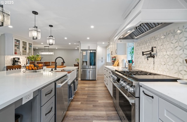 kitchen with wood finished floors, white cabinets, appliances with stainless steel finishes, custom exhaust hood, and decorative light fixtures