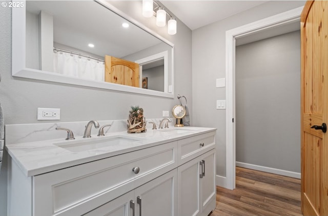 bathroom featuring double vanity, wood finished floors, a sink, and baseboards