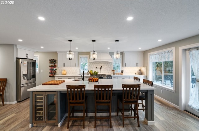 kitchen featuring beverage cooler, stainless steel fridge with ice dispenser, light countertops, white cabinetry, and backsplash