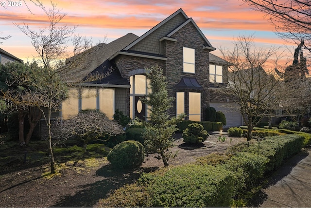 view of front facade with stone siding, an attached garage, and a shingled roof