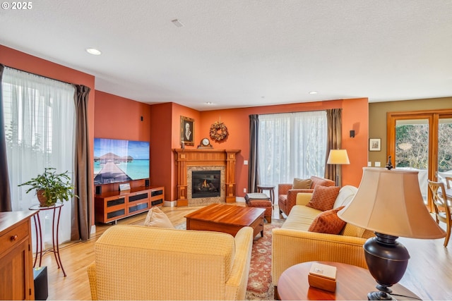 living area with recessed lighting, light wood-style floors, a textured ceiling, and a glass covered fireplace