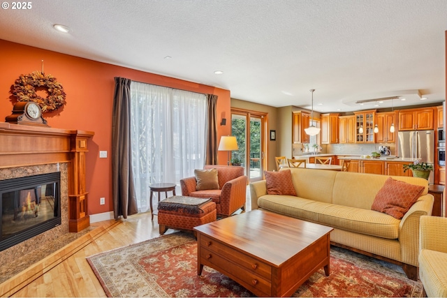 living room featuring baseboards, a premium fireplace, recessed lighting, a textured ceiling, and light wood-type flooring