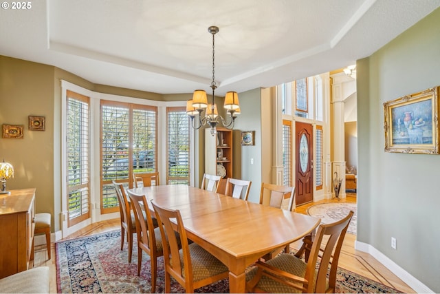 dining area featuring an inviting chandelier, baseboards, and a raised ceiling