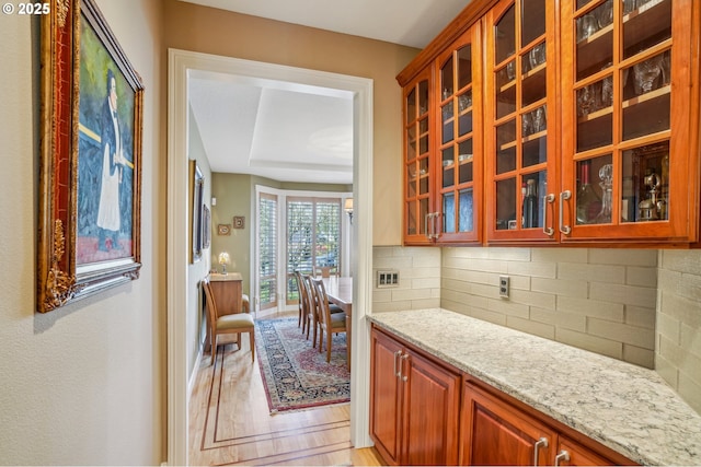 kitchen with decorative backsplash, light wood-style flooring, light stone counters, and glass insert cabinets