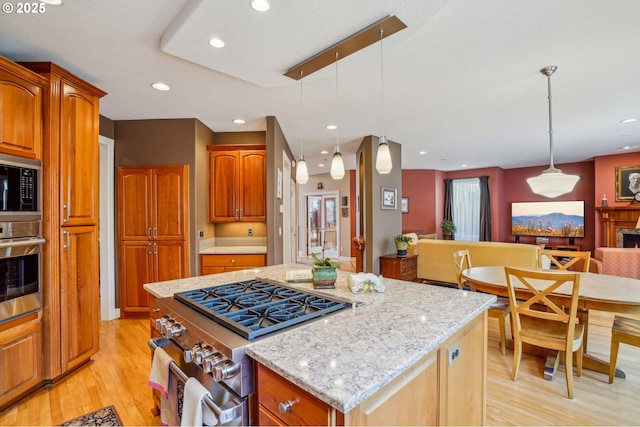 kitchen with open floor plan, a center island, appliances with stainless steel finishes, light wood finished floors, and light stone countertops