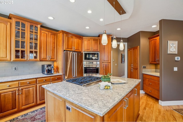 kitchen with light stone countertops, light wood finished floors, glass insert cabinets, appliances with stainless steel finishes, and a center island