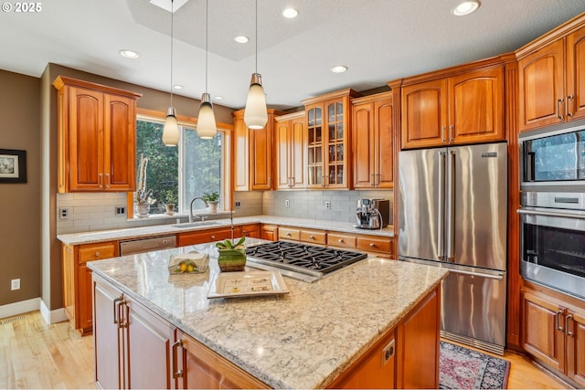 kitchen featuring light stone countertops, a kitchen island, a sink, stainless steel appliances, and glass insert cabinets