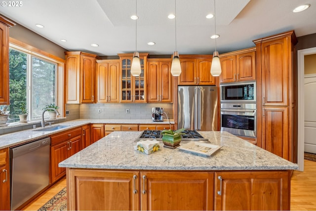 kitchen featuring a kitchen island, light wood-style flooring, appliances with stainless steel finishes, brown cabinetry, and a sink