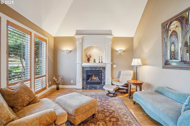 living area featuring a premium fireplace, baseboards, light wood-style floors, and vaulted ceiling