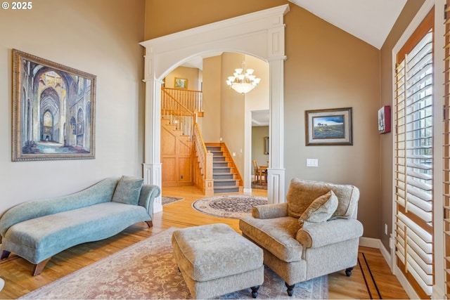 sitting room featuring stairway, wood finished floors, high vaulted ceiling, arched walkways, and a notable chandelier