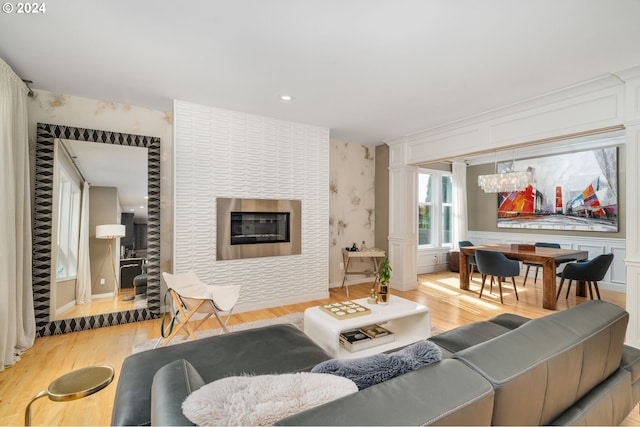 living room with light wood finished floors, wallpapered walls, an inviting chandelier, a fireplace, and a decorative wall