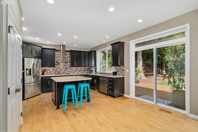 kitchen featuring visible vents, a kitchen island, a kitchen bar, stainless steel appliances, and wall chimney exhaust hood